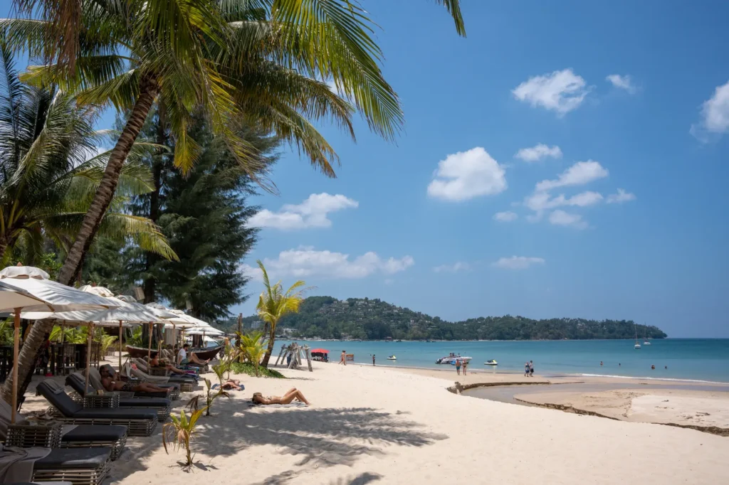 Bang Tao Beach in Phuket with sun loungers, palm trees and a headland