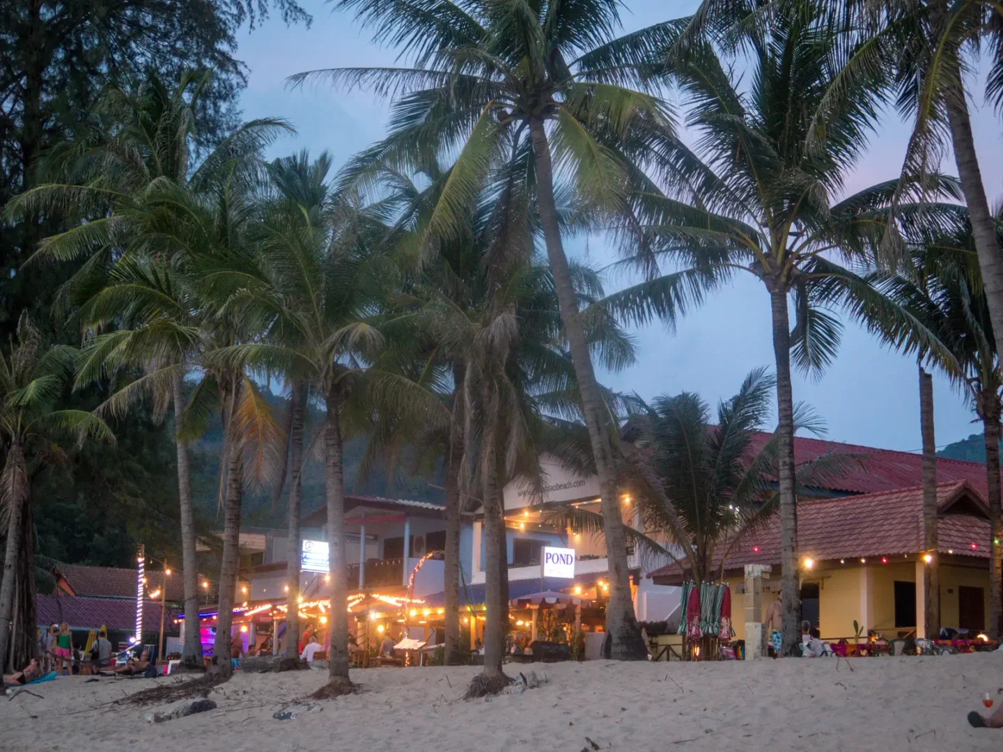 Beachfront restaurants under palm trees on Kamala Beach, Phuket, at dusk